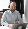 Mitarbeiter mit Headset arbeitet lächelnd am Laptop und unterstützt Kunden im digitalen Support.